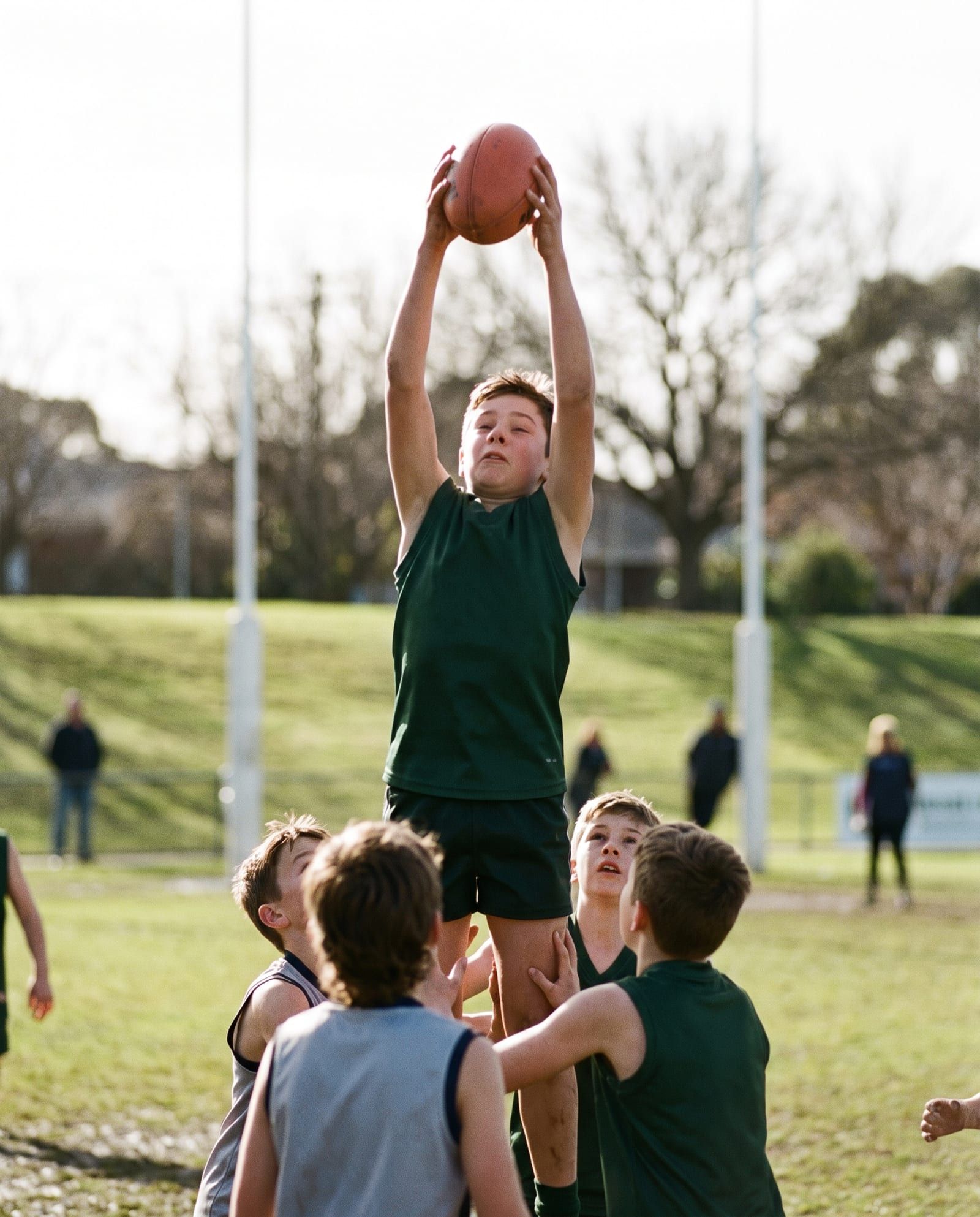 A boy takes a high mark above a pack at a suburban oval, white goal posts behind