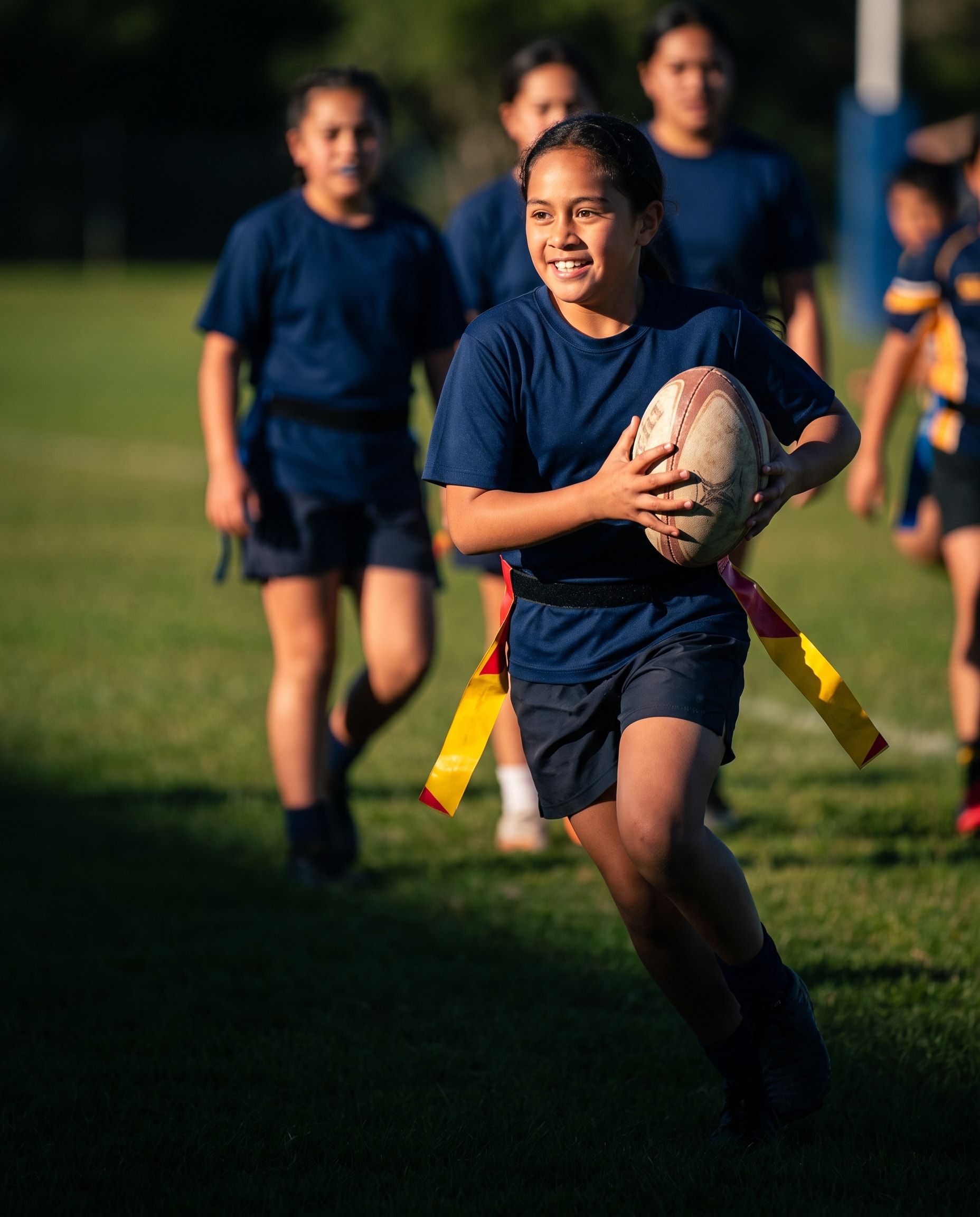 A girl in a tag belt runs into space holding the rugby ball in both hands